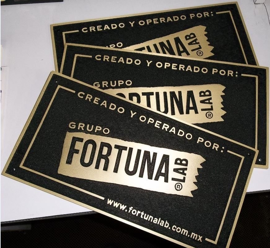 Tres placas fundidas en bronce de Grupo Fortuna Lab con la leyenda «Creado y operado por» y el logotipo en relieve